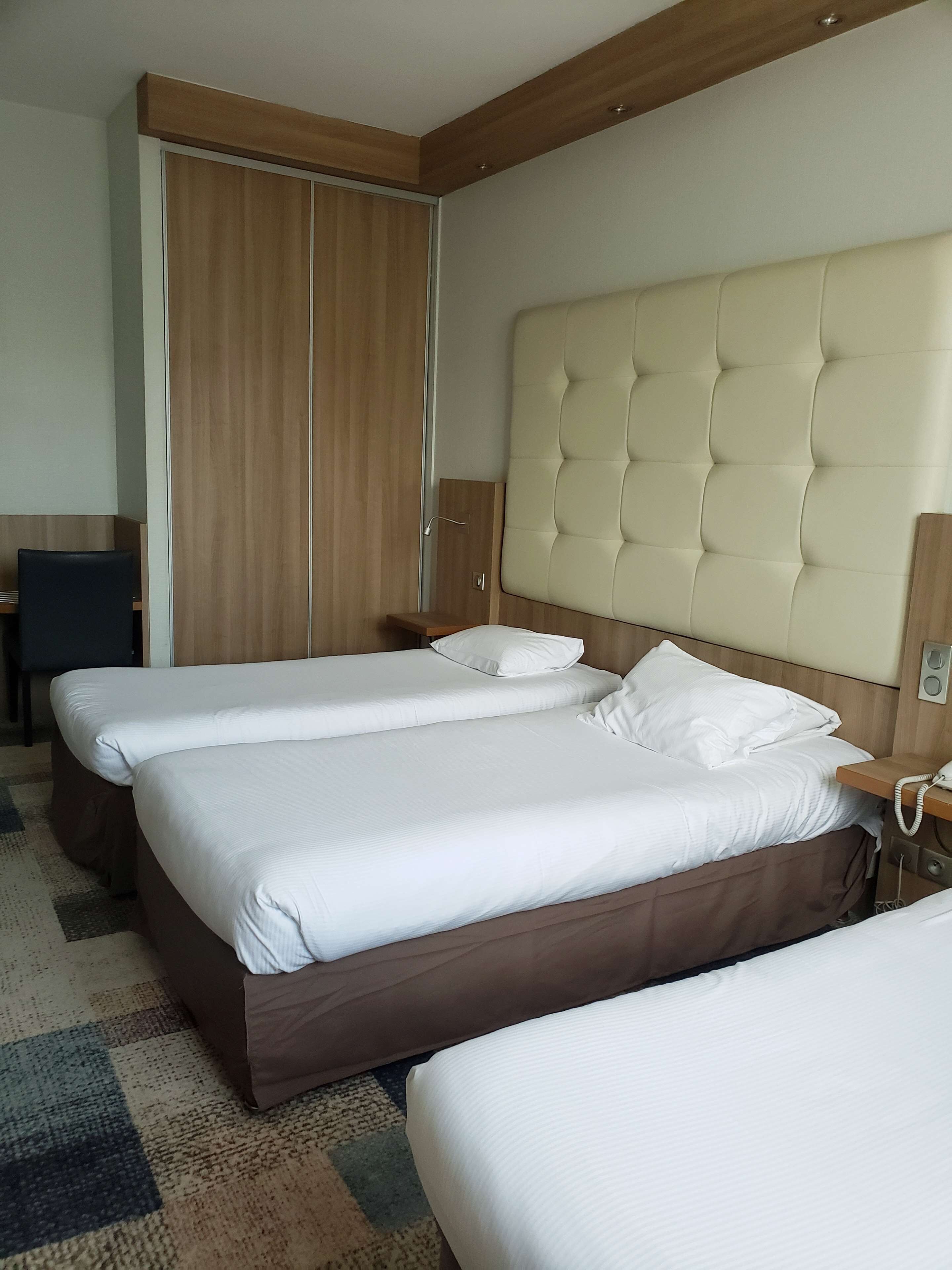 Une chambre d’hôtel avec deux lits, une armoire en bois, un bureau et un téléphone.