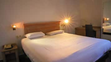 A hotel room with a large bed, two bedside lamps, a nightstand with a telephone, and a mirror on the wall.