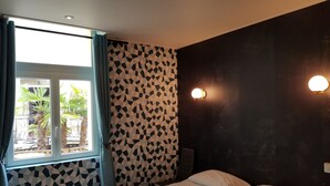 A bedroom with a bed, a window with curtains, a patterned wall, and two wall-mounted lights.