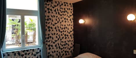 A bedroom with a bed, a window with curtains, a patterned wall, and two wall-mounted lights.