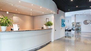 A modern reception area with a curved reception desk, potted plants, and a clean, tiled floor. - Idea Hotel Piacenza (Piacenza)