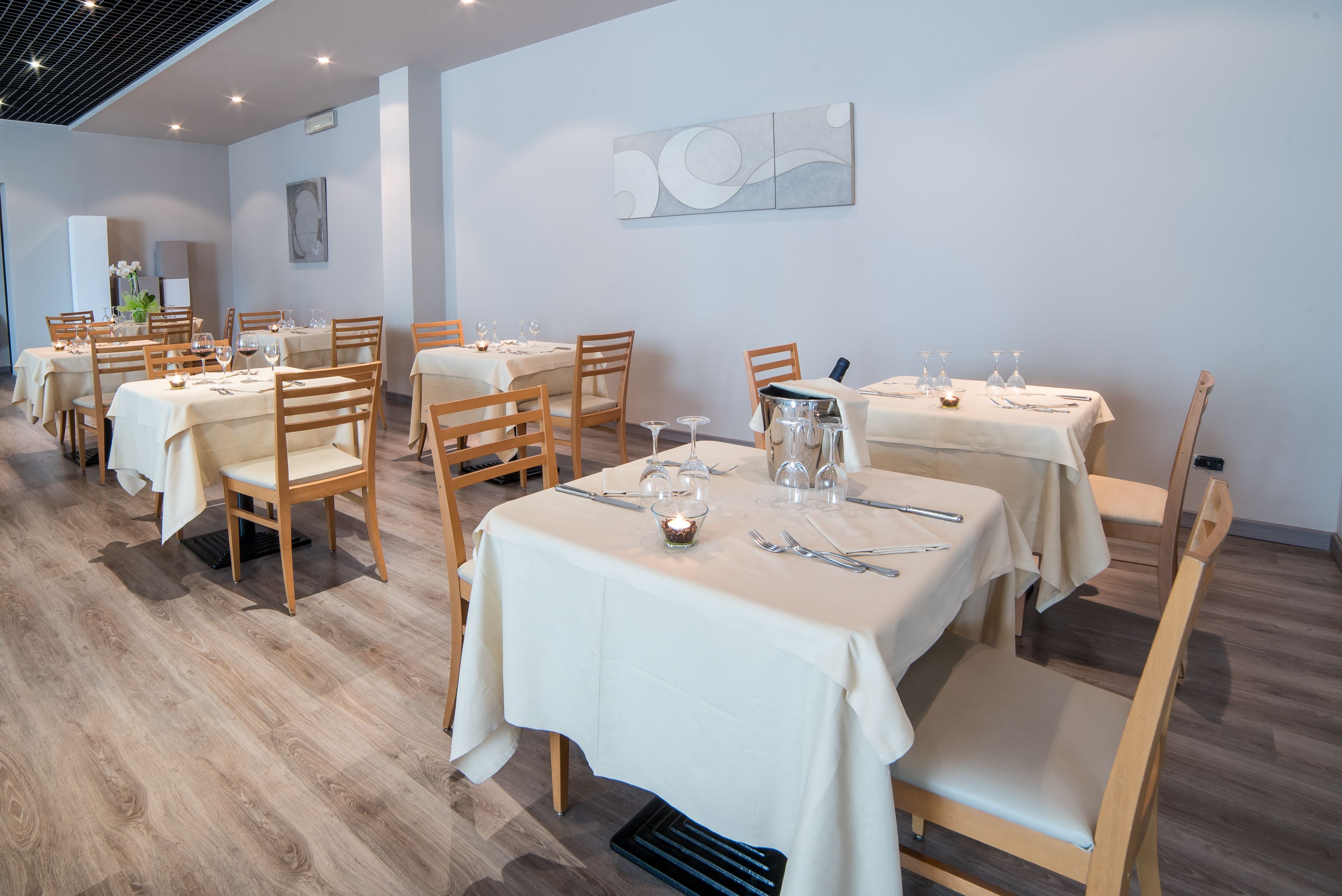Een restaurant met meerdere tafels, klaar voor diners, met houten stoelen en witte tafellakens.