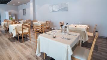 Un restaurante con varias mesas dispuestas para comer, con sillas de madera y manteles blancos.
