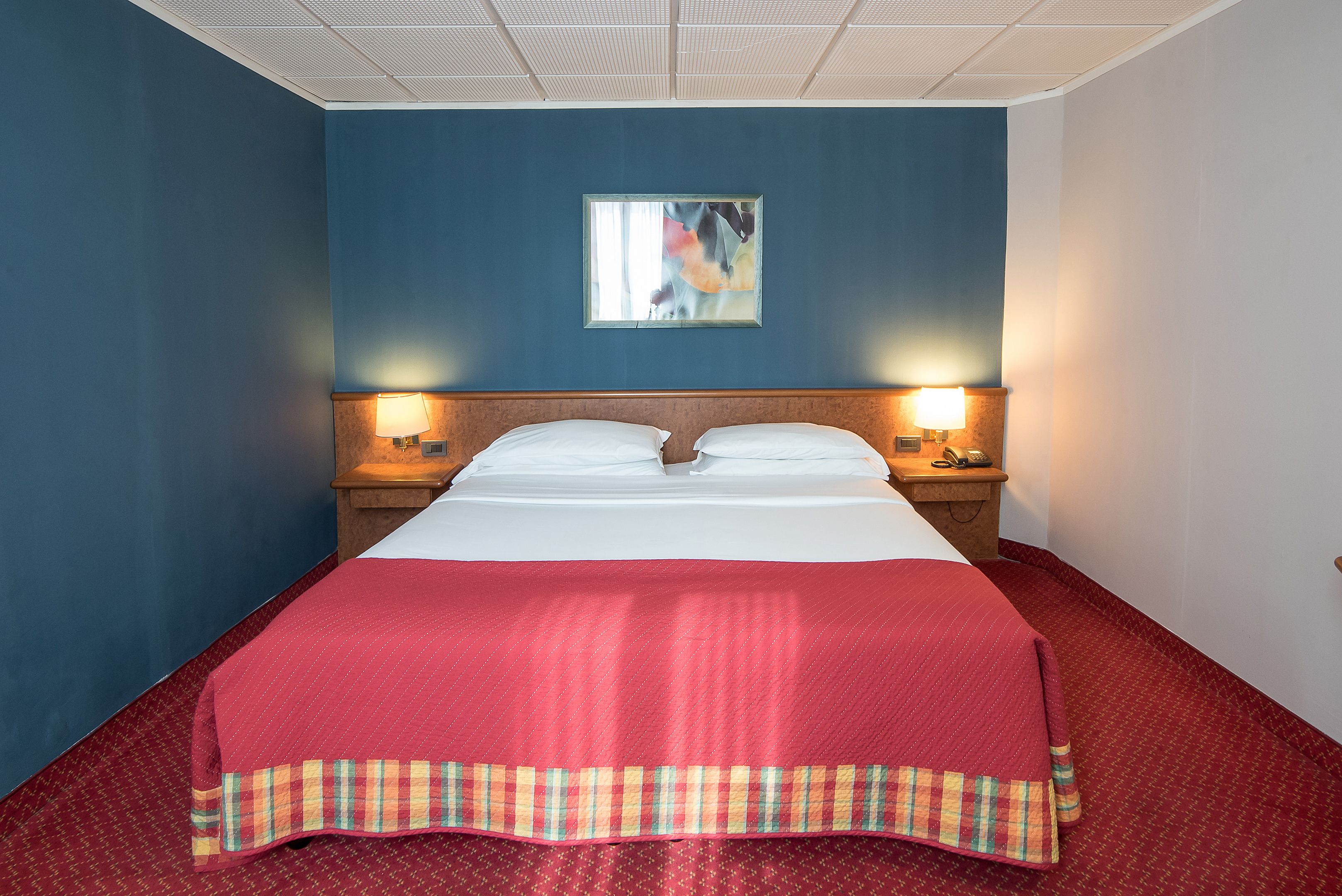 A hotel room with a large bed, two bedside lamps, a nightstand, and a wall-mounted picture.