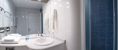 A modern bathroom with a white sink, a large mirror, and a blue-tiled shower area.
