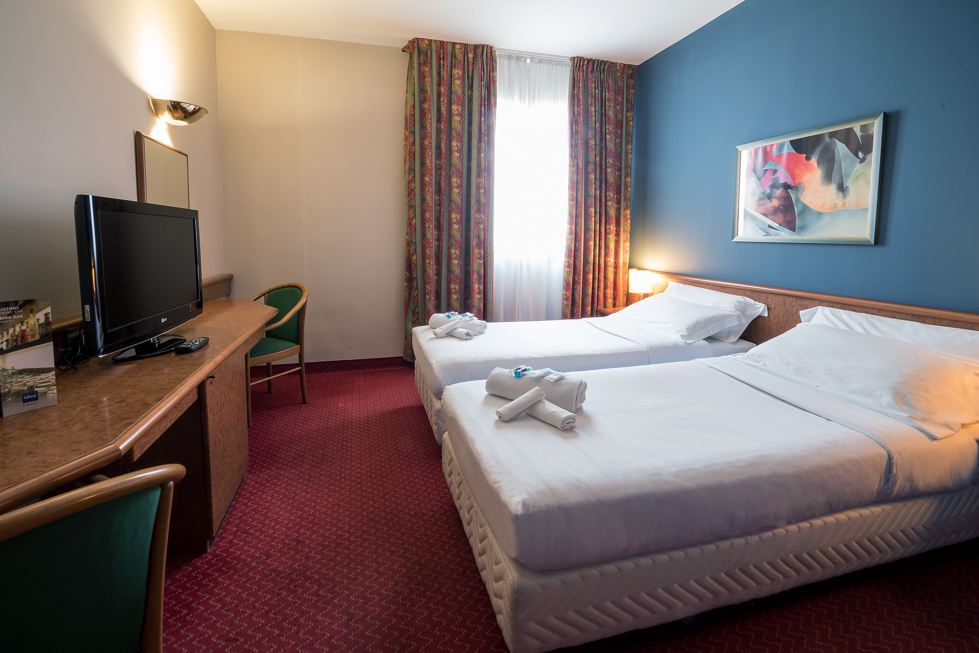 Ein Hotelzimmer mit zwei Betten, einem Schreibtisch mit Fernseher und einem Sessel.