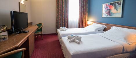 Ein Hotelzimmer mit zwei Betten, einem Schreibtisch mit Fernseher und einem Sessel.