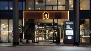 L'ingresso moderno di un hotel con reception, porte in vetro e una segnaletica che elenca servizi come ristorante e bar/lounge.