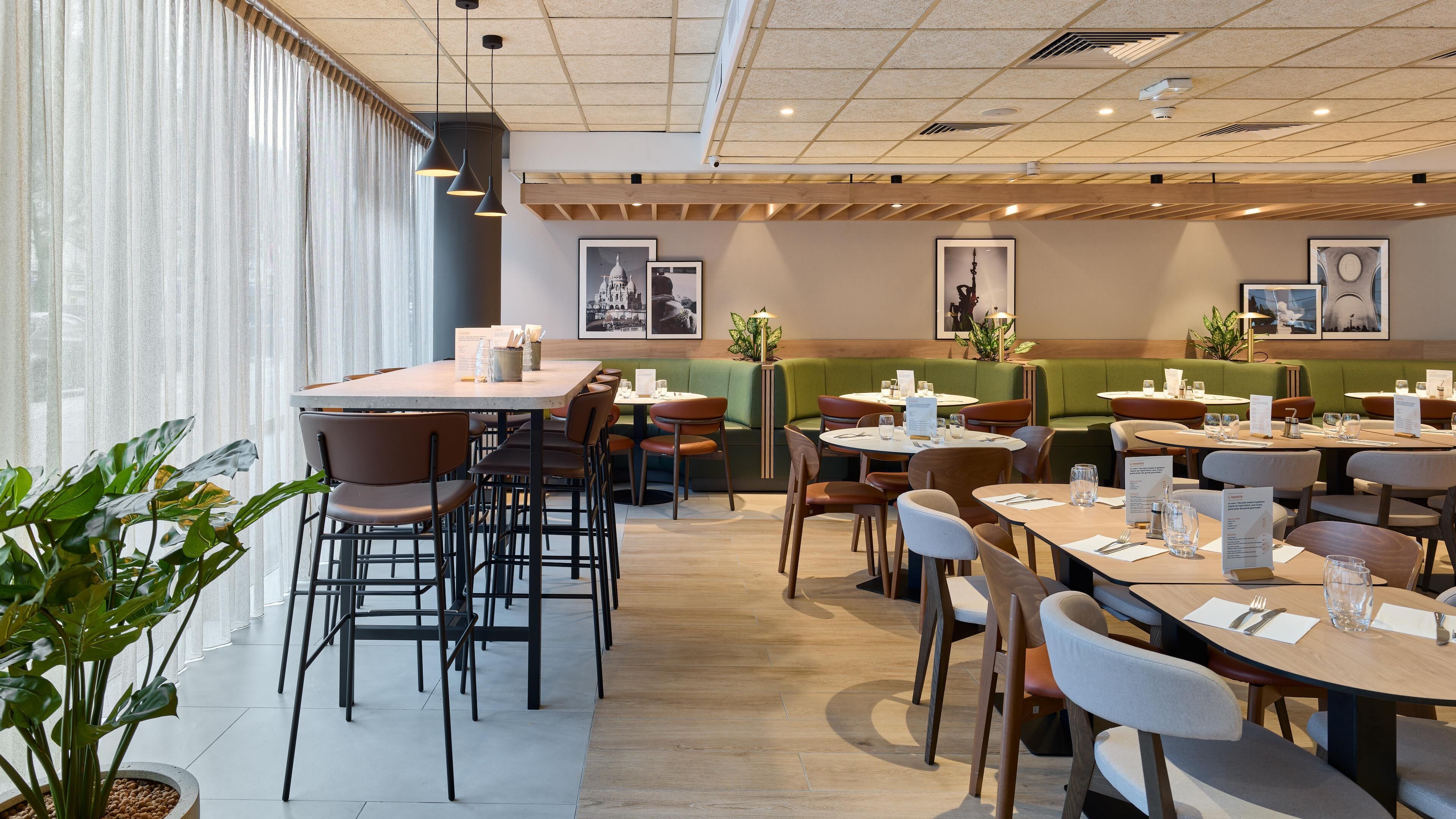 Een modern restaurant met hoge tafels en zitbanken, houten balken in het plafond en ingelijste kunstwerken aan de wanden.