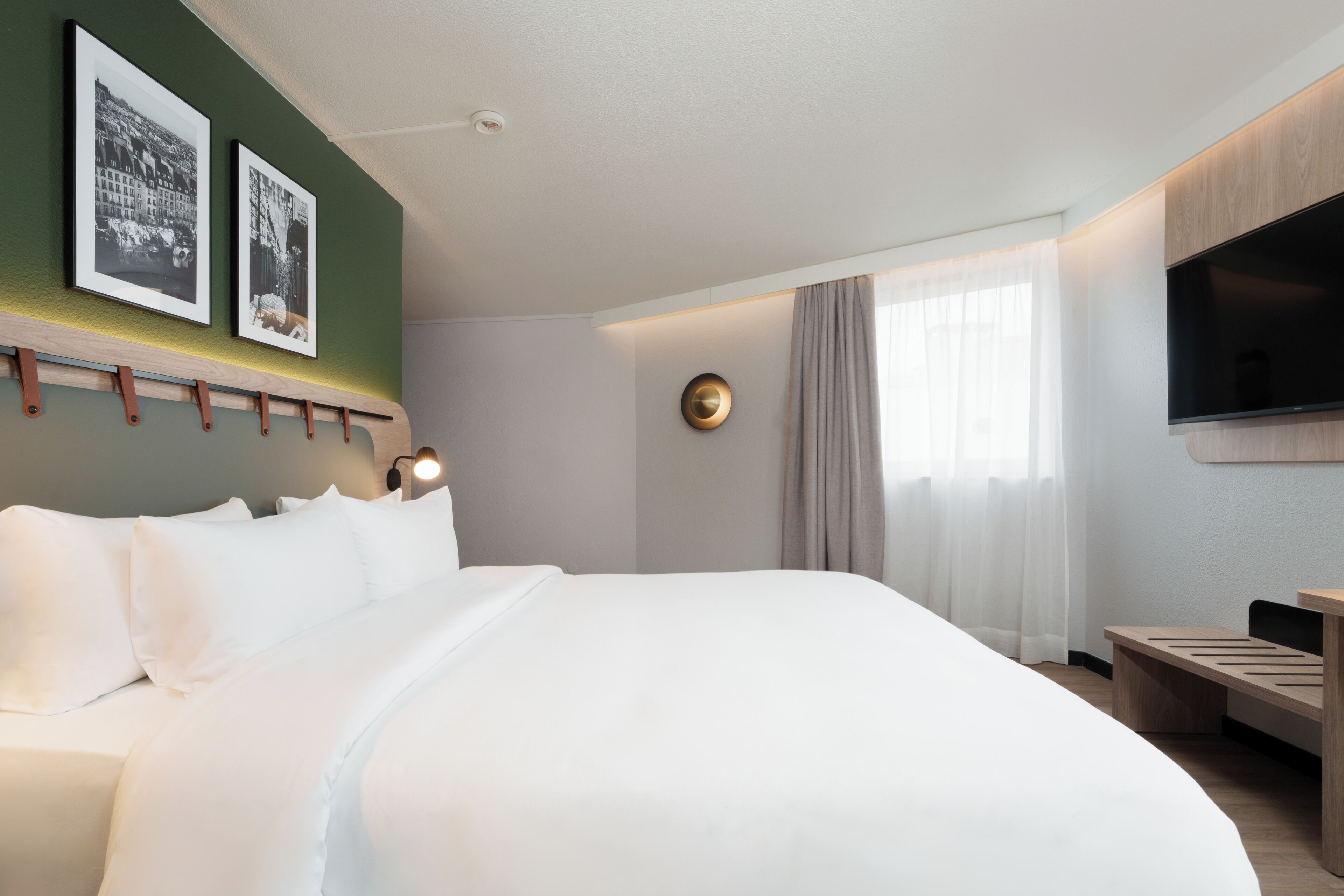 Une chambre d’hôtel moderne, dotée d’un grand lit, d’un bureau, d’une télévision à écran plat et de deux tableaux encadrés accrochés au mur.