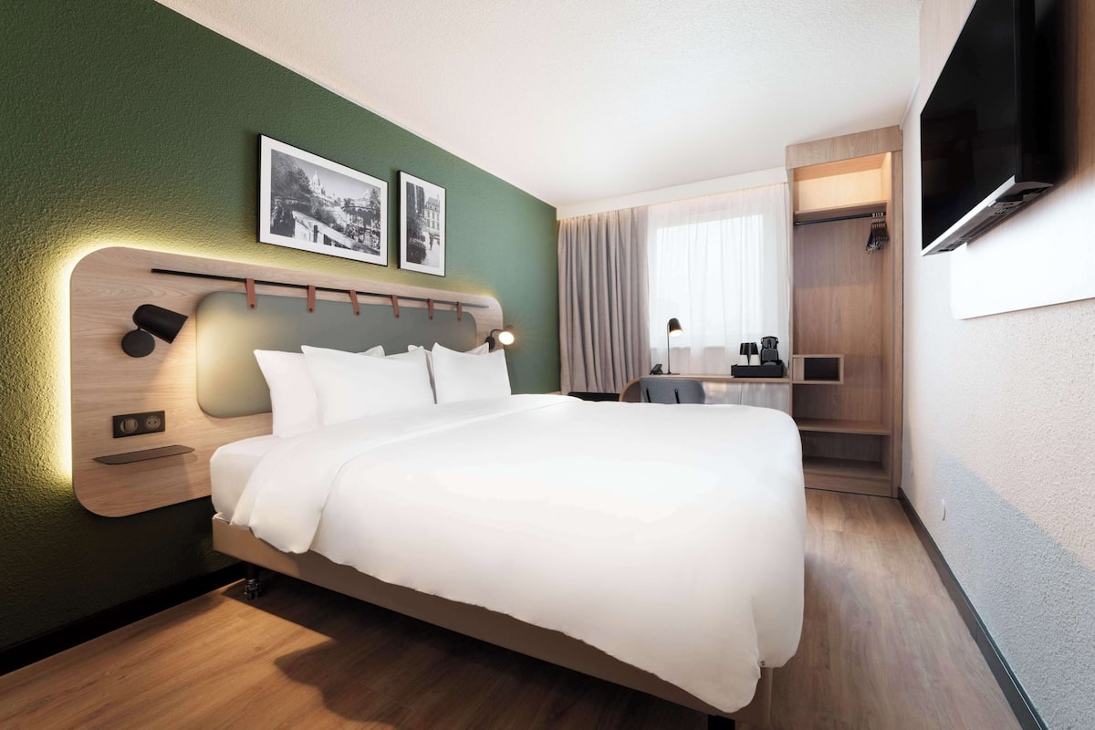 Ein modernes Hotelzimmer mit einem großen Bett, einem Schreibtisch und einem Fernseher.
