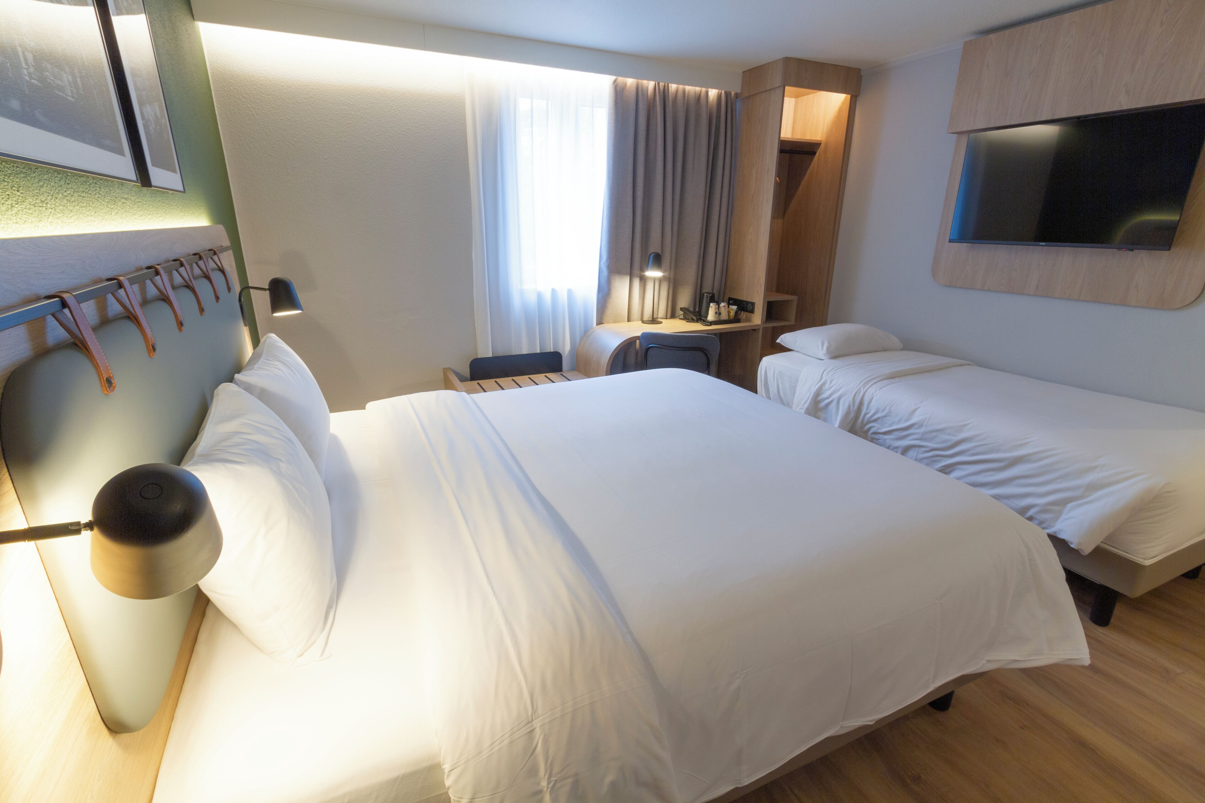A hotel room with two beds, a desk, a chair, a TV, and a window with curtains.