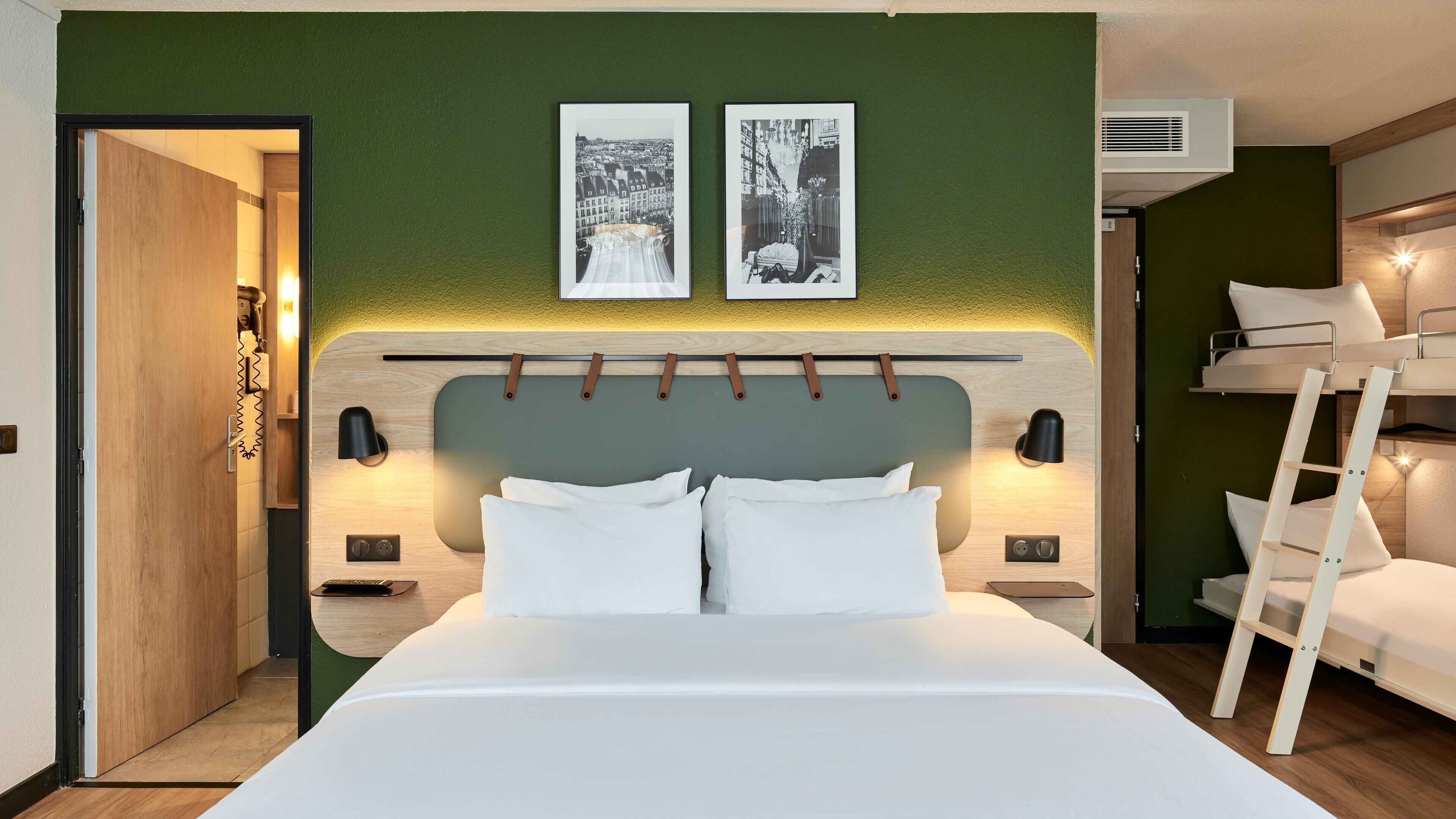 A modern hotel room with a large bed, a bunk bed, and two framed pictures on the wall.