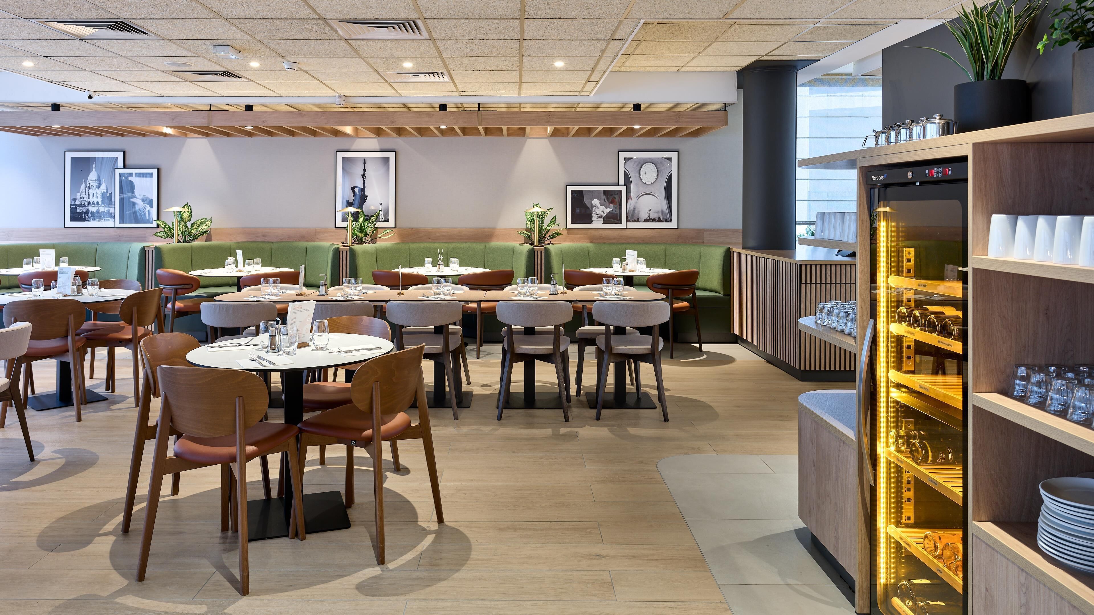 A restaurant with round tables and chairs, a coffee machine, and framed pictures on the walls.