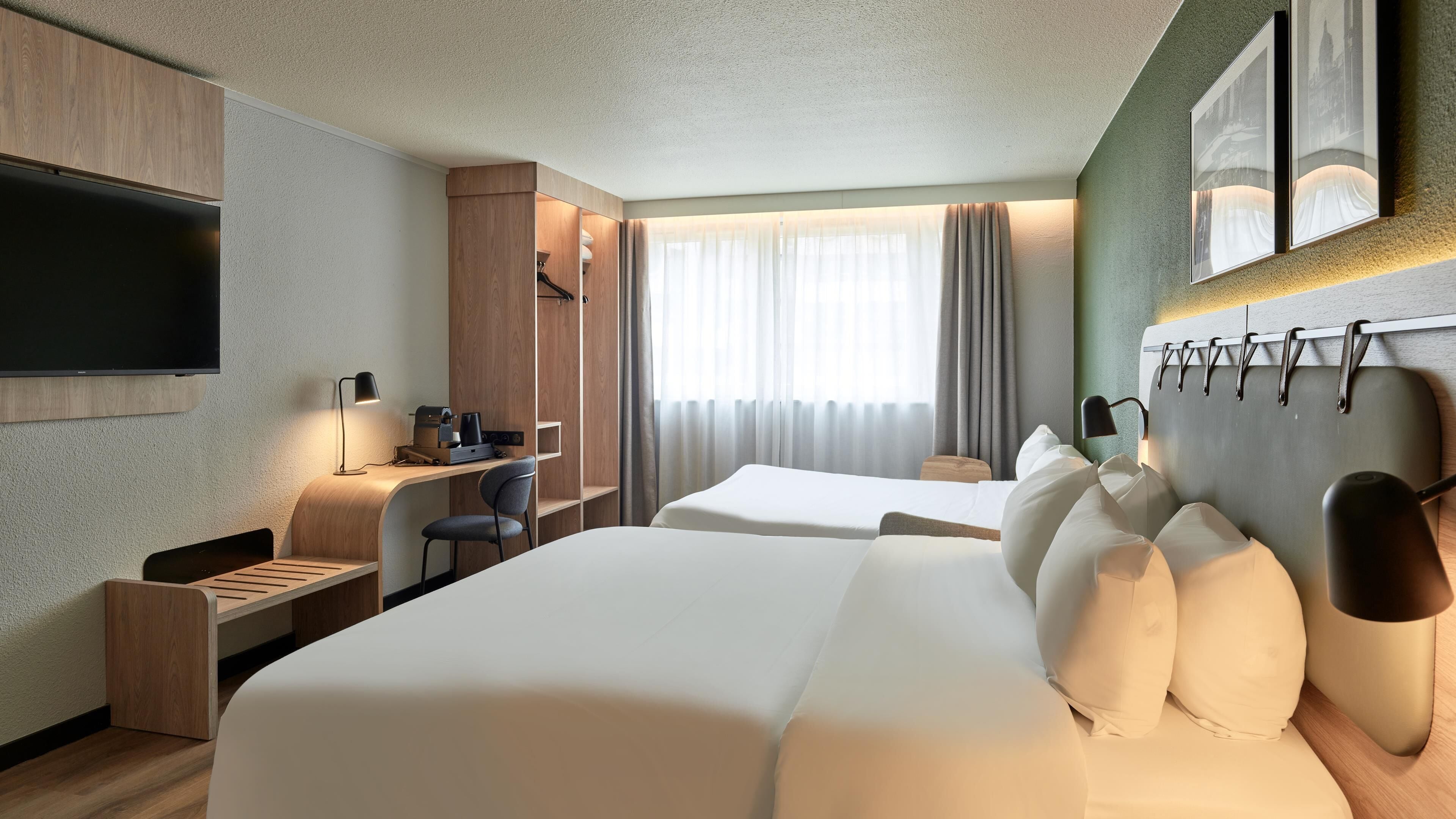 Une chambre d’hôtel avec un grand lit, un bureau avec une chaise, un téléviseur à écran plat et une fenêtre avec des rideaux.