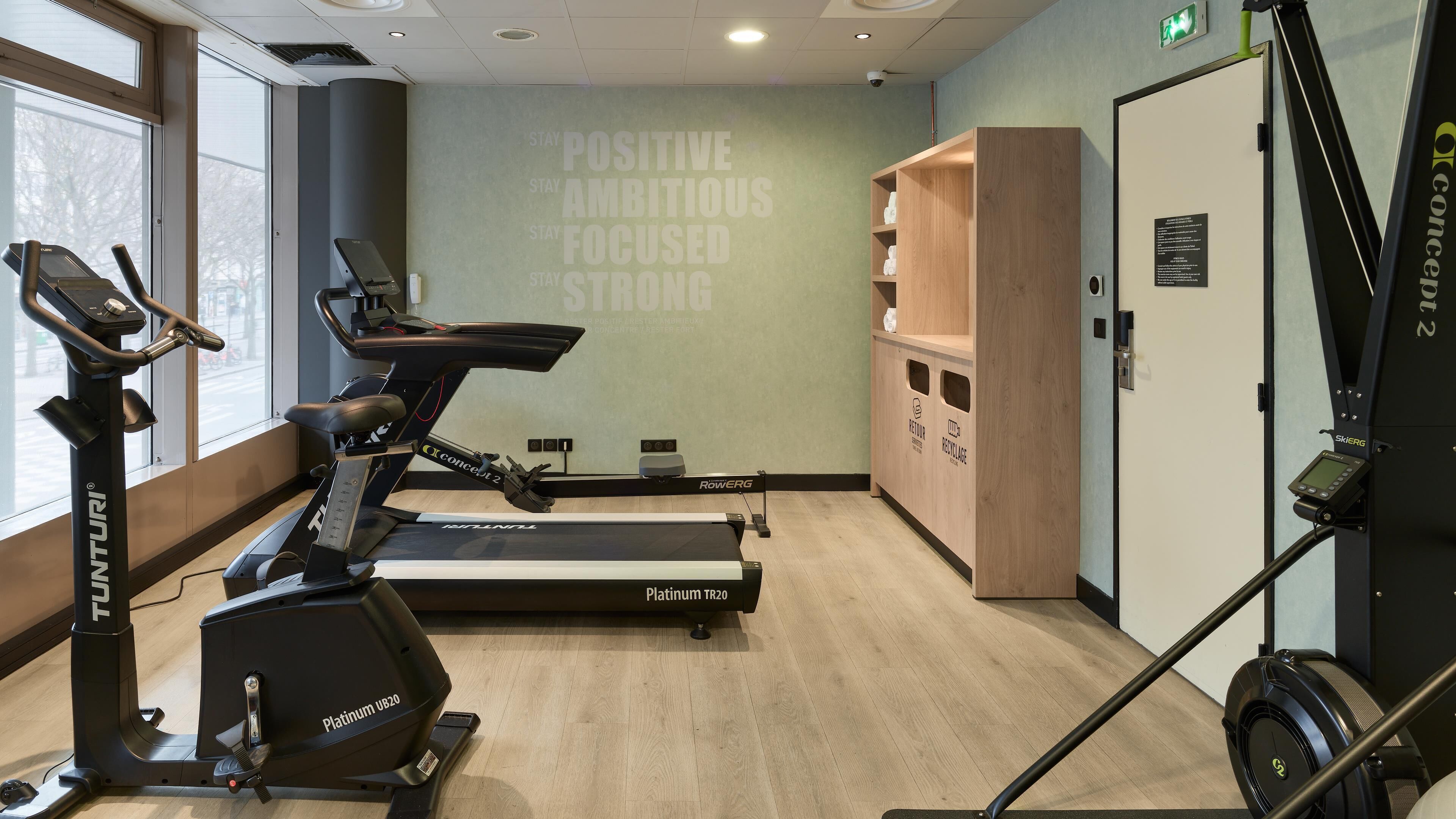 Ein Fitnessraum mit Trainingsgeräten, motivierenden Wandtexten und einem Holzschrank mit Recyclingbehältern.