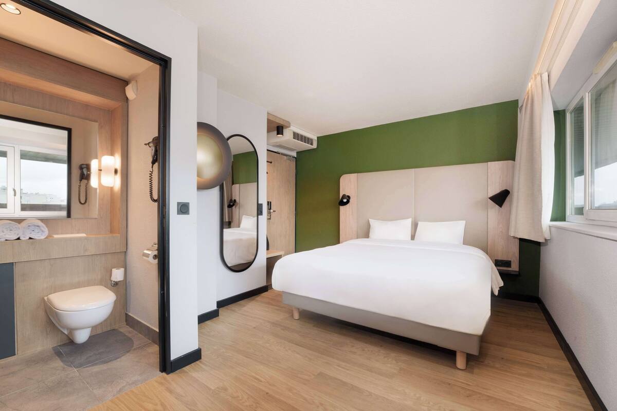 Ein modernes Hotelzimmer mit einem großen Bett, einem Badezimmer mit Toilette und Spiegel sowie einer Wand in Grünton.