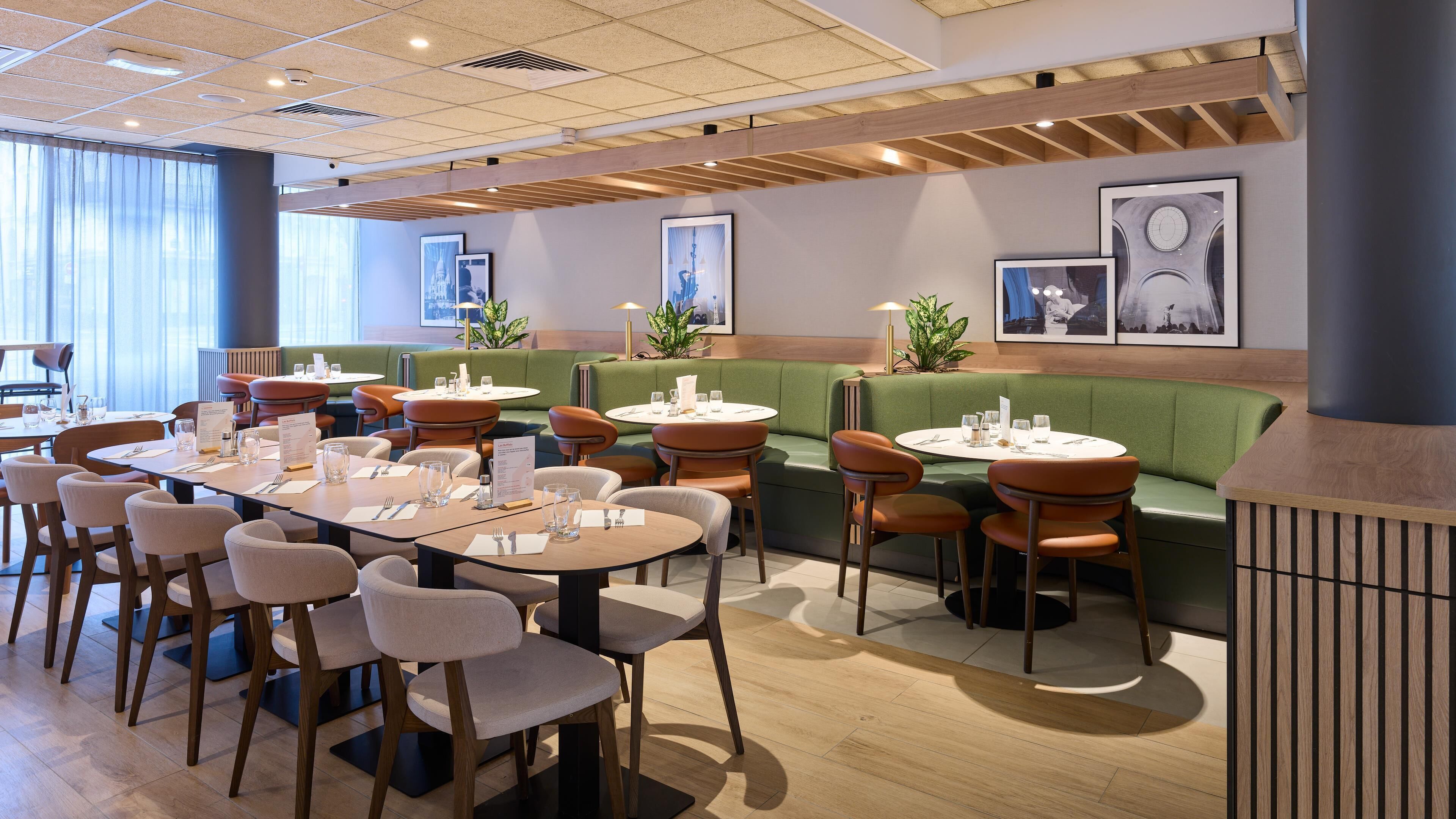 A modern restaurant with round tables, green cushioned seating, and wooden accents.