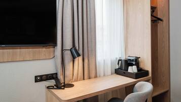 Habitación de hotel con un escritorio de madera, un televisor de pantalla plana, una lámpara, una cafetera y una silla.