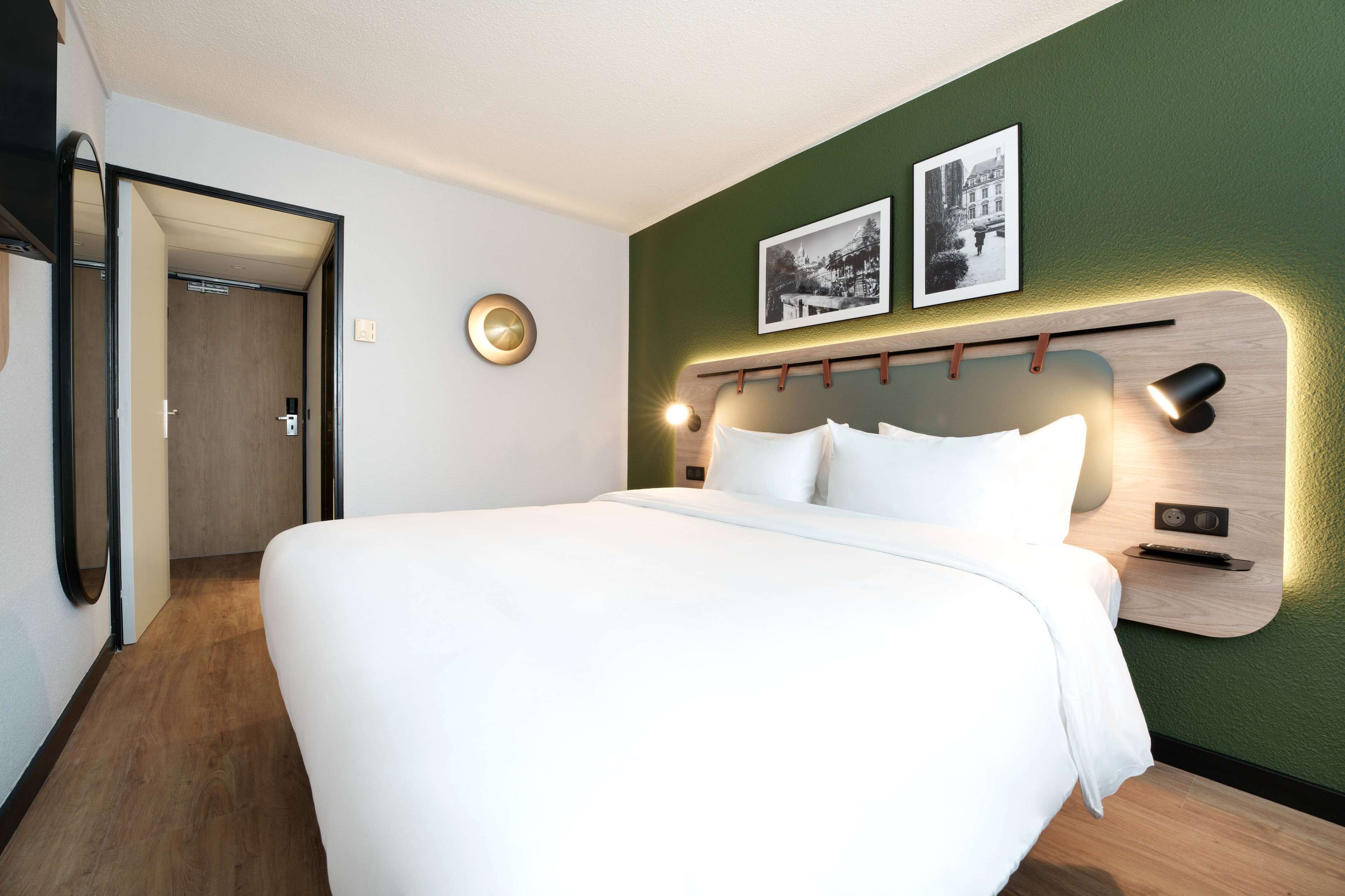 A modern hotel room with a large bed, a wooden headboard, and two framed pictures on the wall.