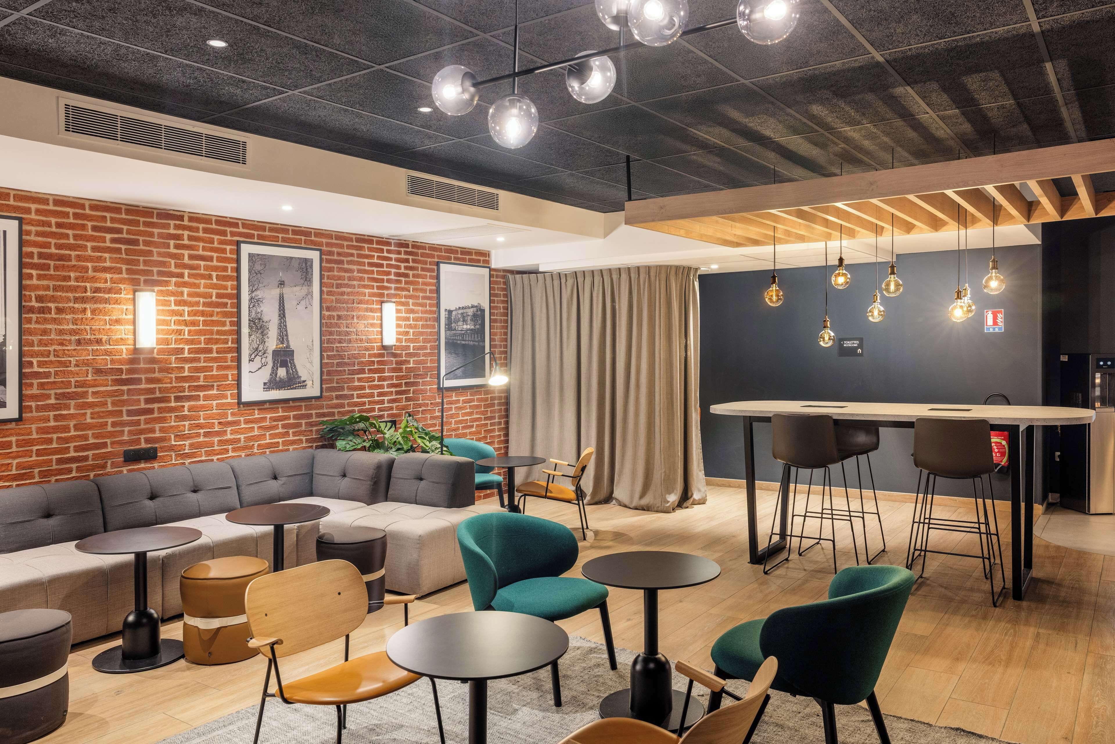 A modern lounge area with a brick wall, seating arrangements, and pendant lighting.