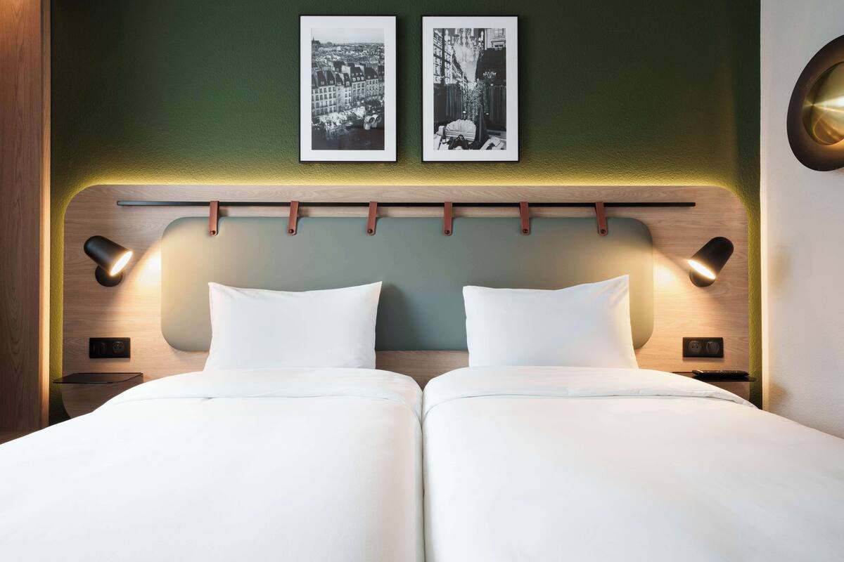 Ein Doppelbett mit zwei Kissen, ein Kopfteil mit einer Leuchte und zwei gerahmte Bilder an der Wand.
