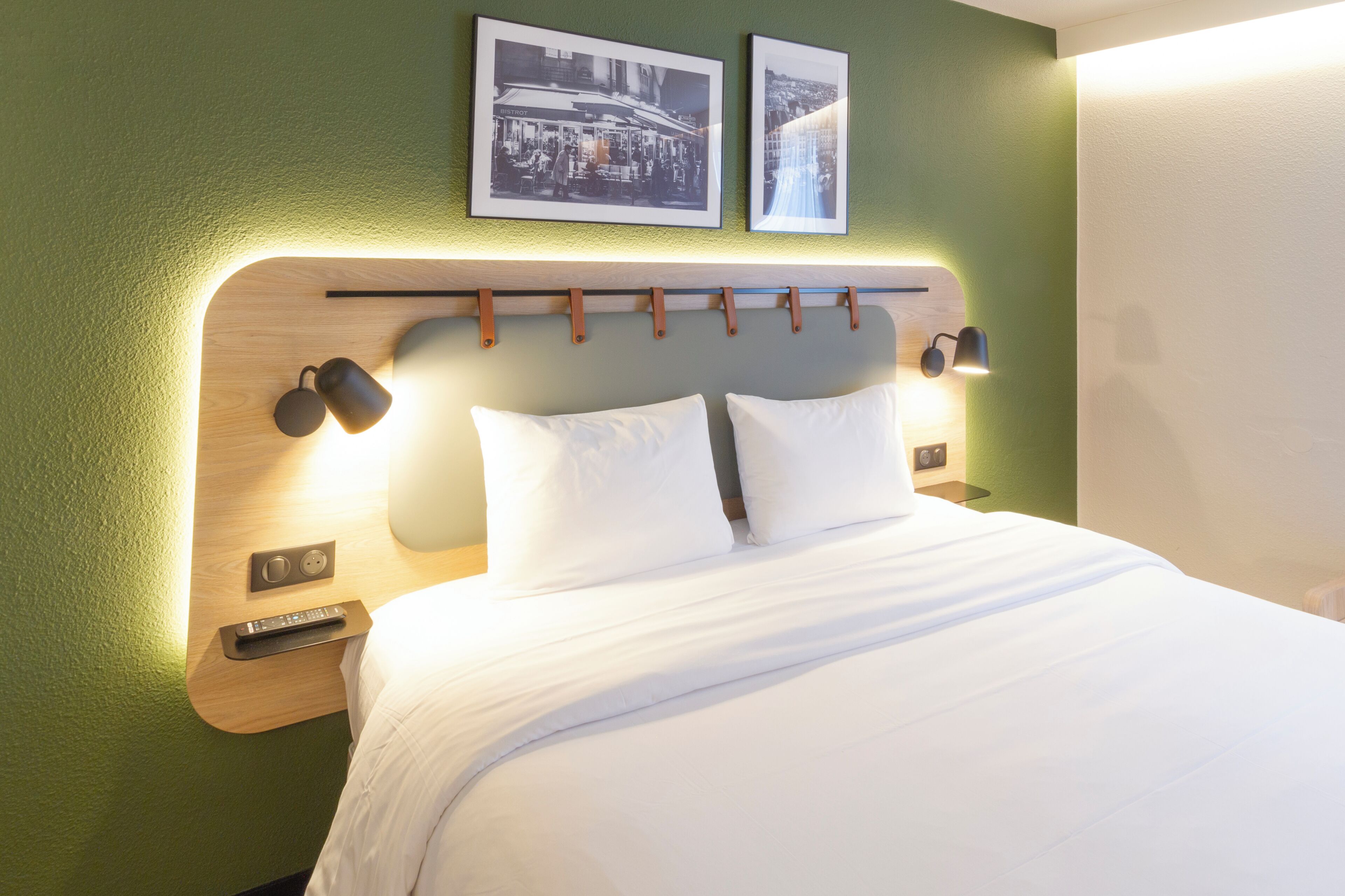 A neatly made bed with white linens, a wooden headboard with built-in lighting, and two framed pictures on the wall above.