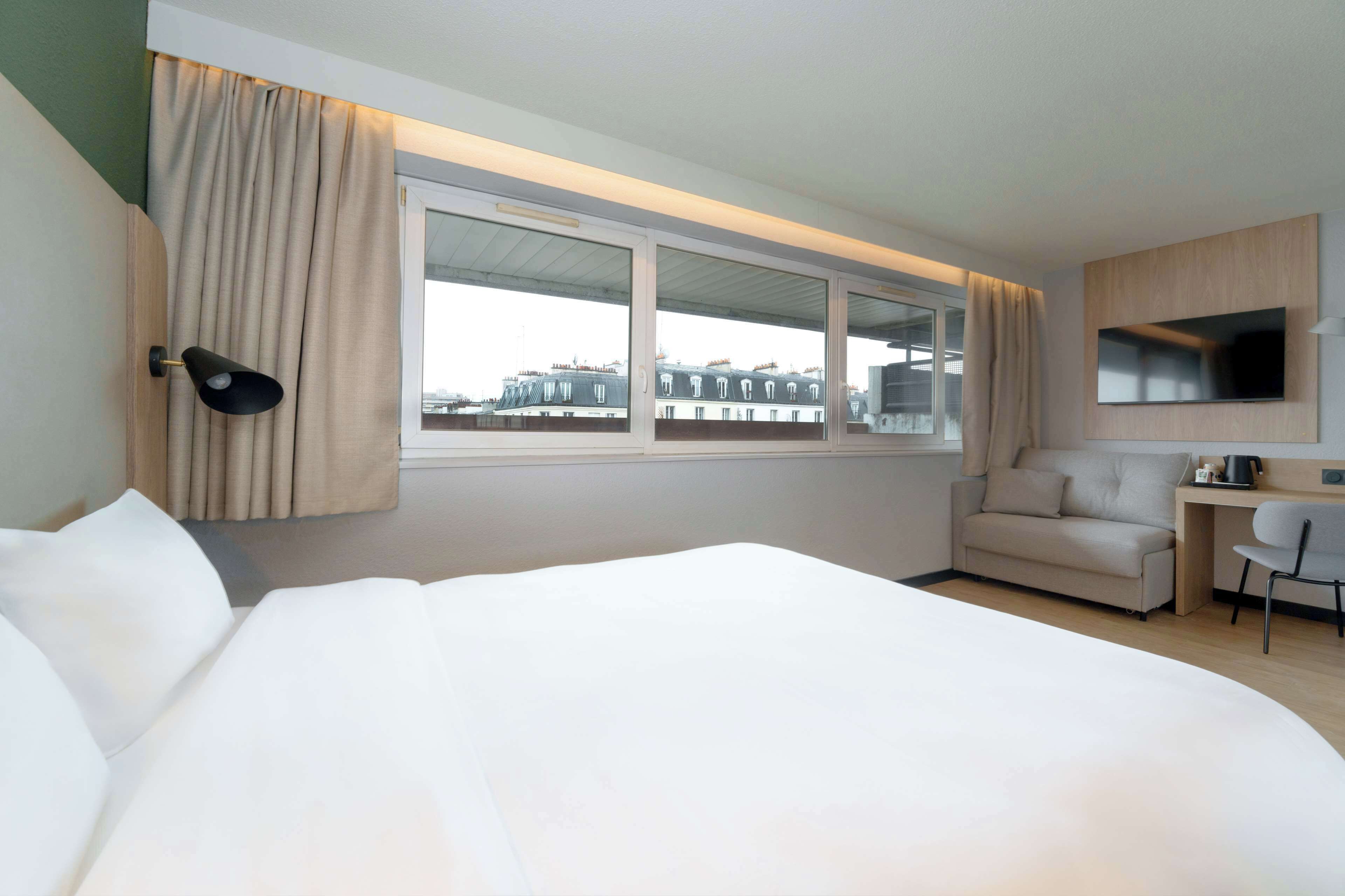 A hotel room with a large bed, a desk, a chair, a TV, and a window with curtains.