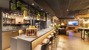 Zona bar moderna con bancone, sgabelli e schermo televisivo.