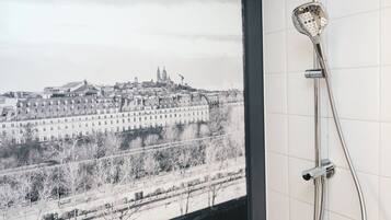 Une salle de bain équipée d’une baignoire, d’une douche et offrant une vue sur le paysage urbain par une fenêtre.