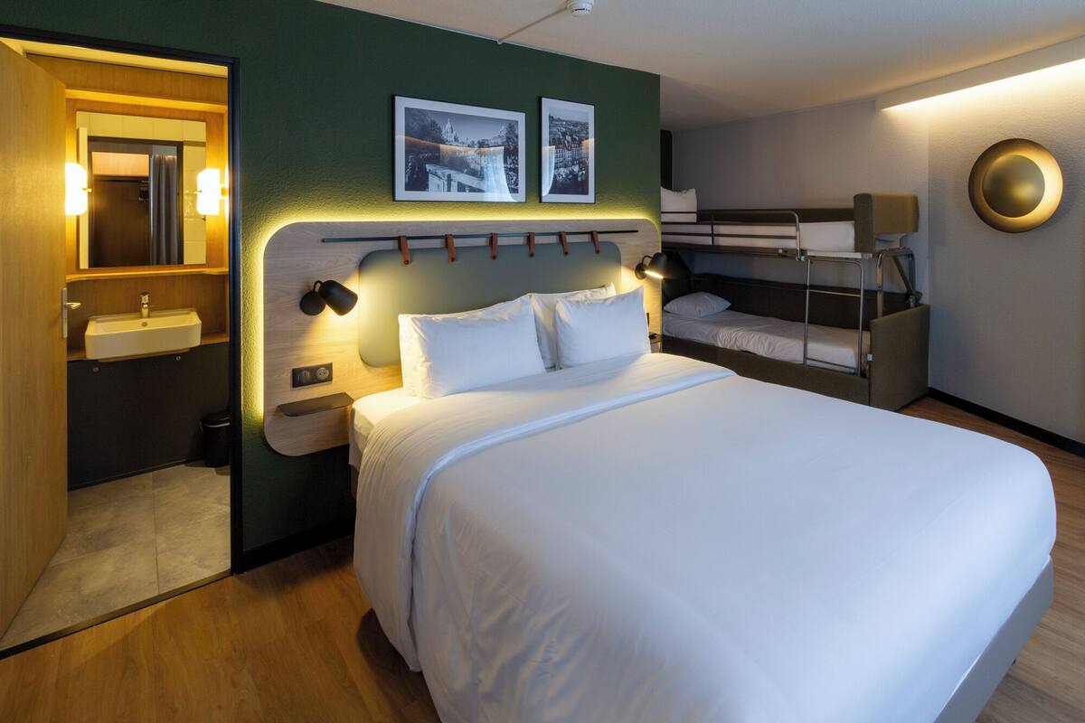 Ein Hotelzimmer mit einem großen Bett, einem Nachttisch, einem Spiegel, einem Waschbecken und einem Stockbett.