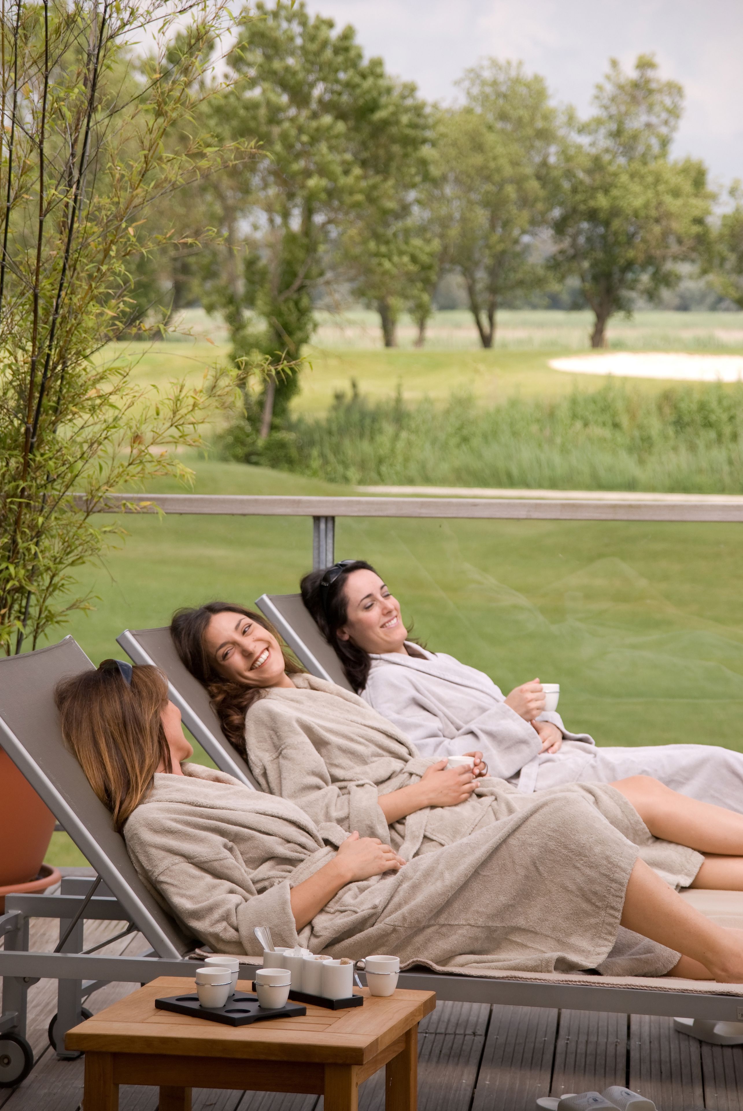 Three people relaxing on lounge chairs in a spa-like setting with a view of a golf course.