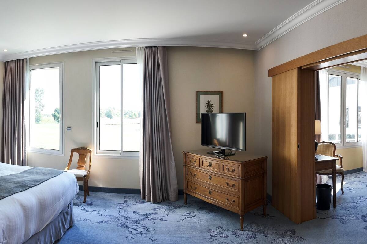 Une chambre d’hôtel avec un grand lit, une télévision, une commode en bois et une chaise.