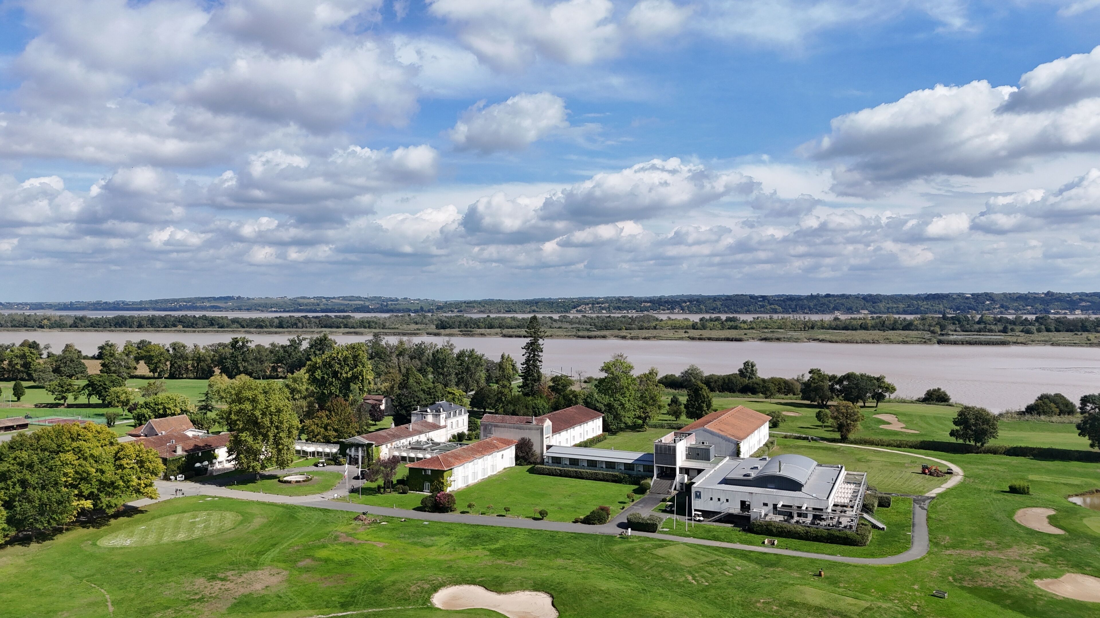 Un campo de golf con un club de campo, un río al fondo y un cielo nublado.