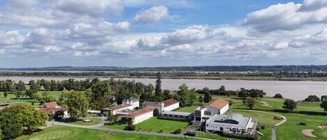 Un campo de golf con un club de campo, un río al fondo y un cielo nublado.