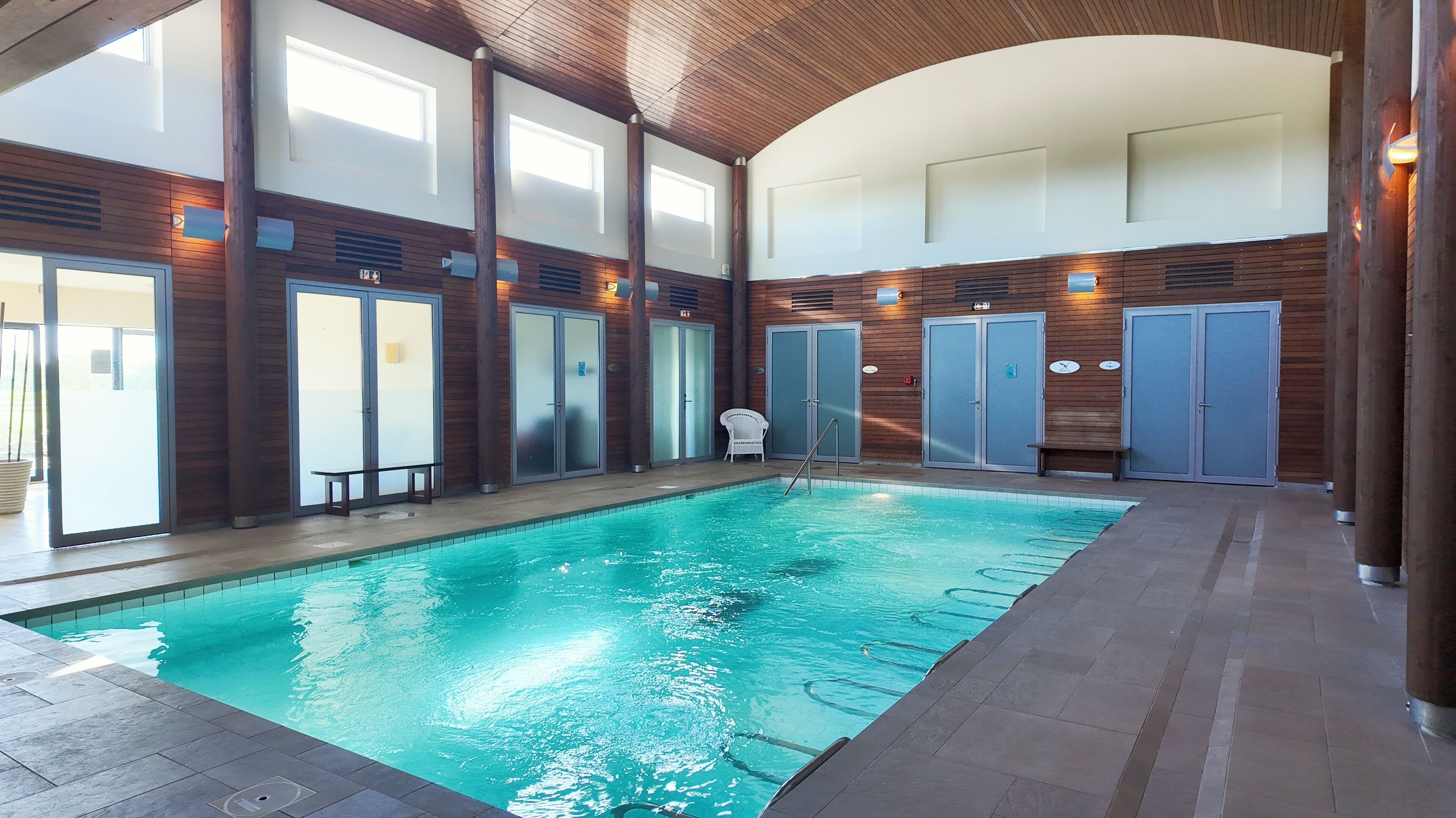 Ein Hallenbad mit klarem Wasser, Holzwandverkleidung und mehreren Türen.