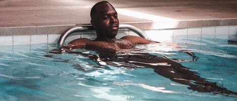A person in a swimming pool with a door and a tiled wall in the background.