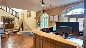 A reception area with a wooden counter, a computer, and a staircase leading to an upper floor. - Relais de Margaux – Hôtel, Golf & Spa (Margaux-Cantenac)