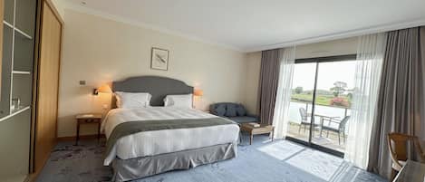 A hotel room with a large bed, a sofa, a small table, and a view of the outdoors.