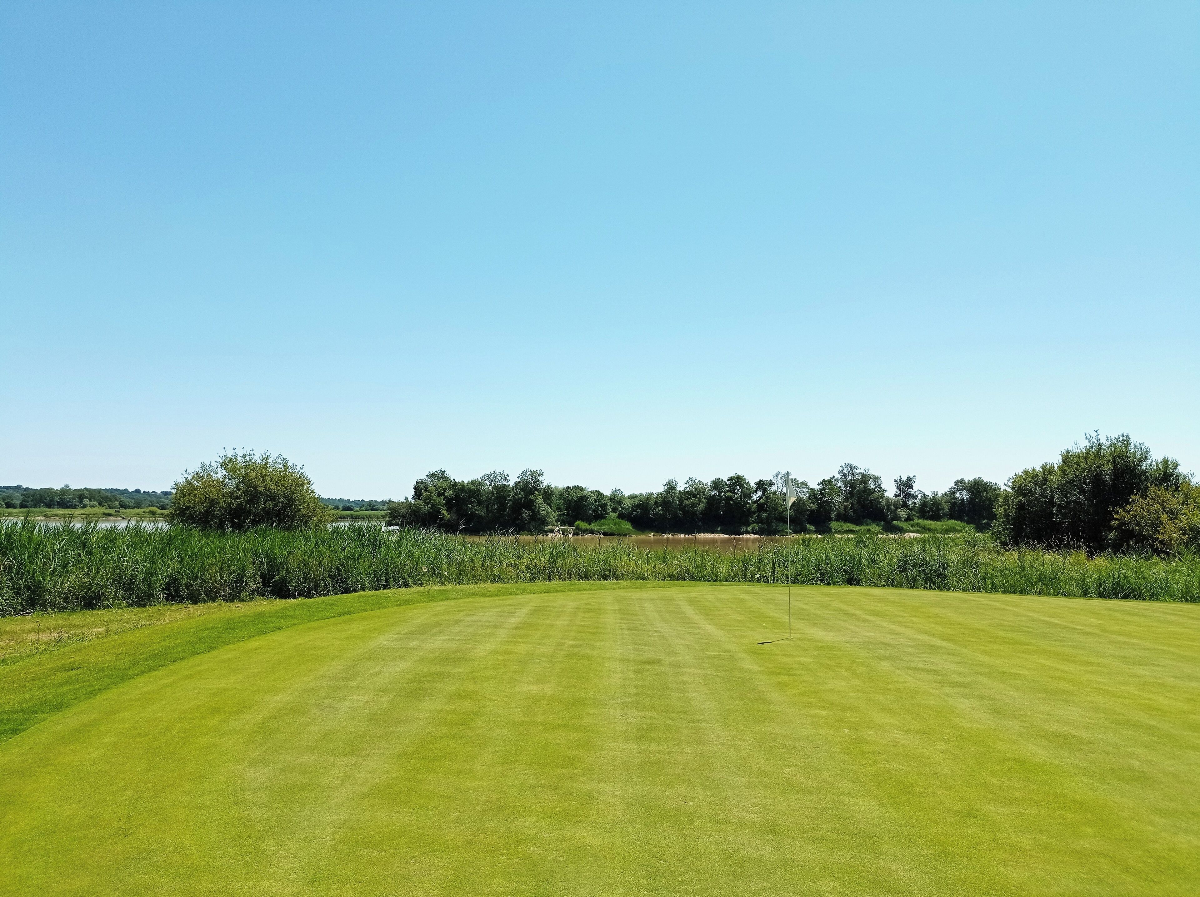 A well-maintained golf course with a clear sky and lush greenery.