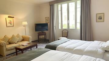 Une chambre d’hôtel avec deux lits, un canapé, un téléviseur posé sur un meuble et une fenêtre avec des rideaux.