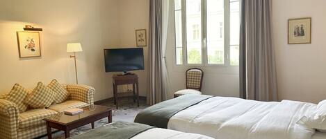 A hotel room with two beds, a sofa, a TV on a stand, and a window with curtains.