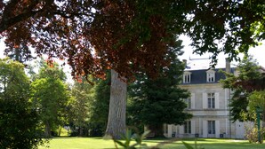A large tree in a well-maintained lawn with a building in the background. - Relais de Margaux – Hôtel, Golf & Spa (Margaux-Cantenac)