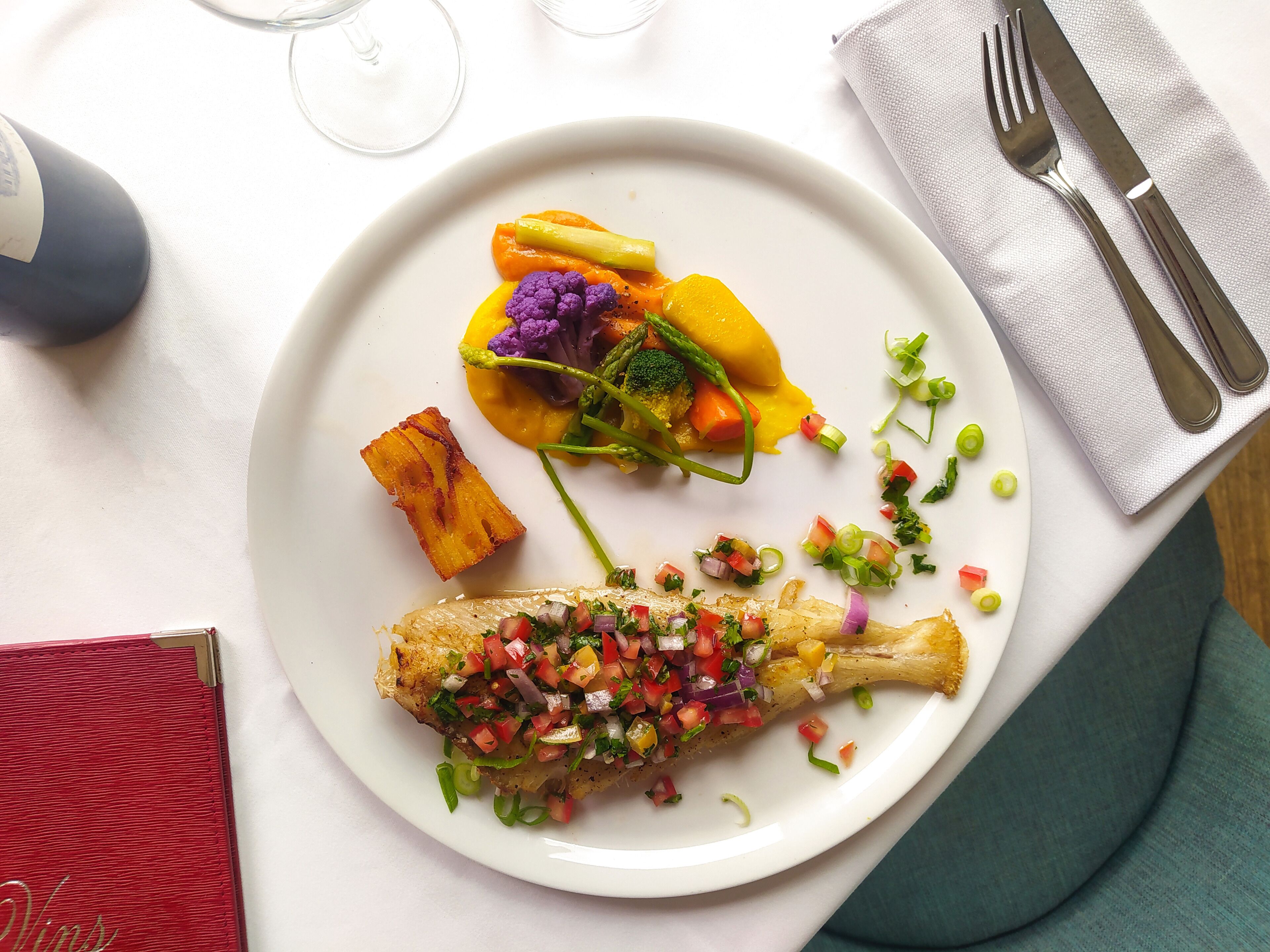 A plate of food with a variety of vegetables and a piece of meat, accompanied by a fork and knife on a napkin.