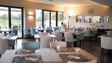 Ein Restaurant mit gedeckten Tischen, großen Fenstern und Zimmerpflanzen.