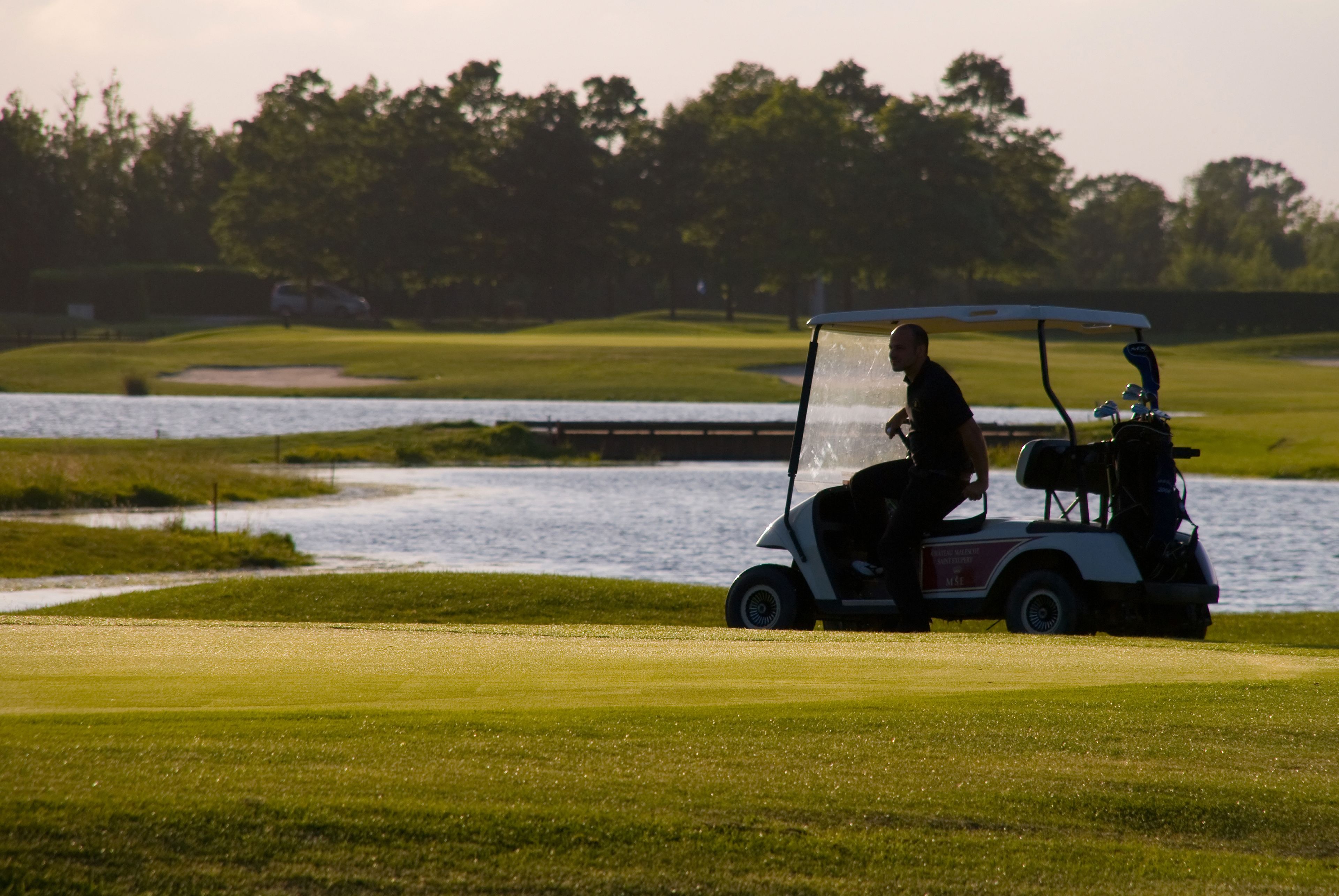 A golf course with a water body and trees in the background.