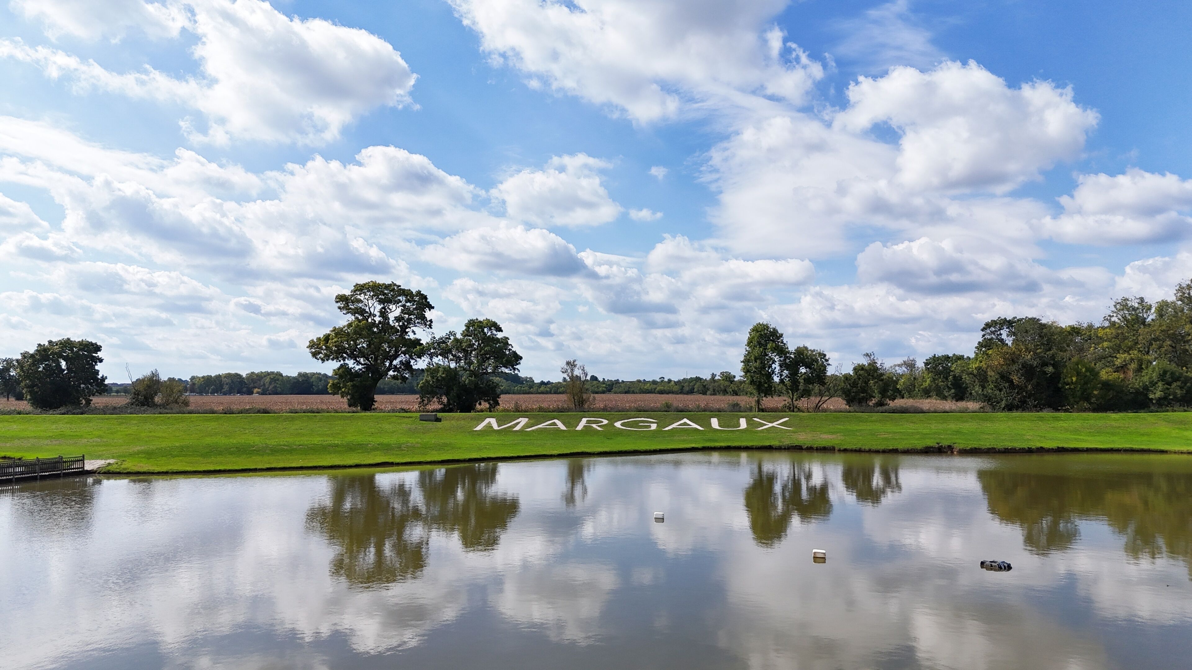 Paesaggio sereno con uno stagno che riflette alberi e cielo, con la scritta "MARGAUX" ben visibile.