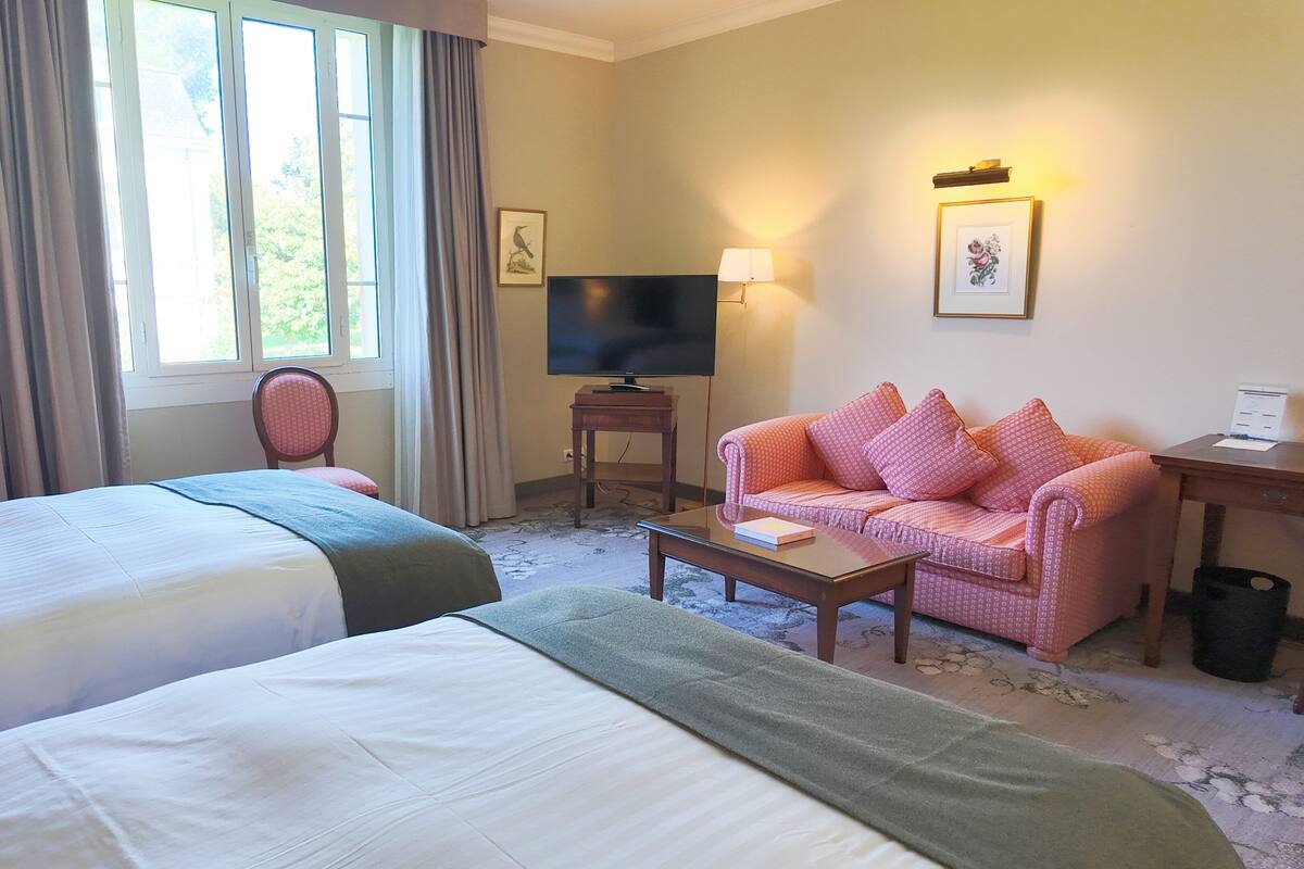 Une chambre d’hôtel avec deux lits simples, un canapé, une télévision et une lampe.