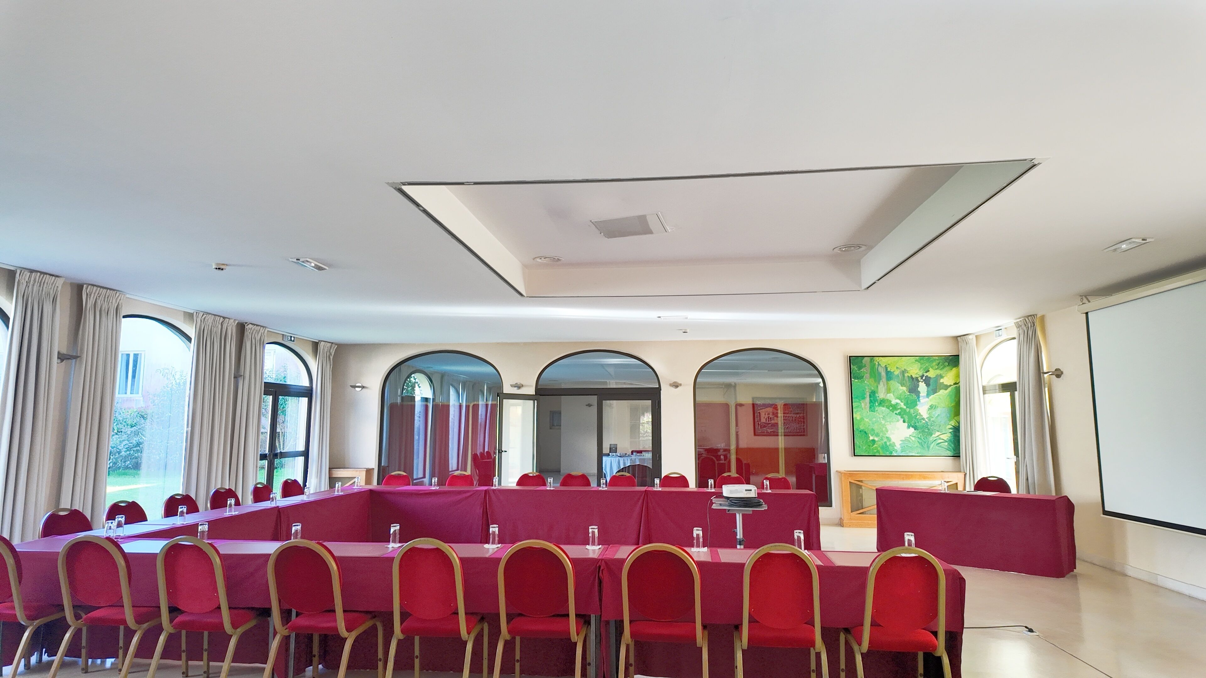 A conference room with multiple tables and chairs, large windows, and a projector screen.