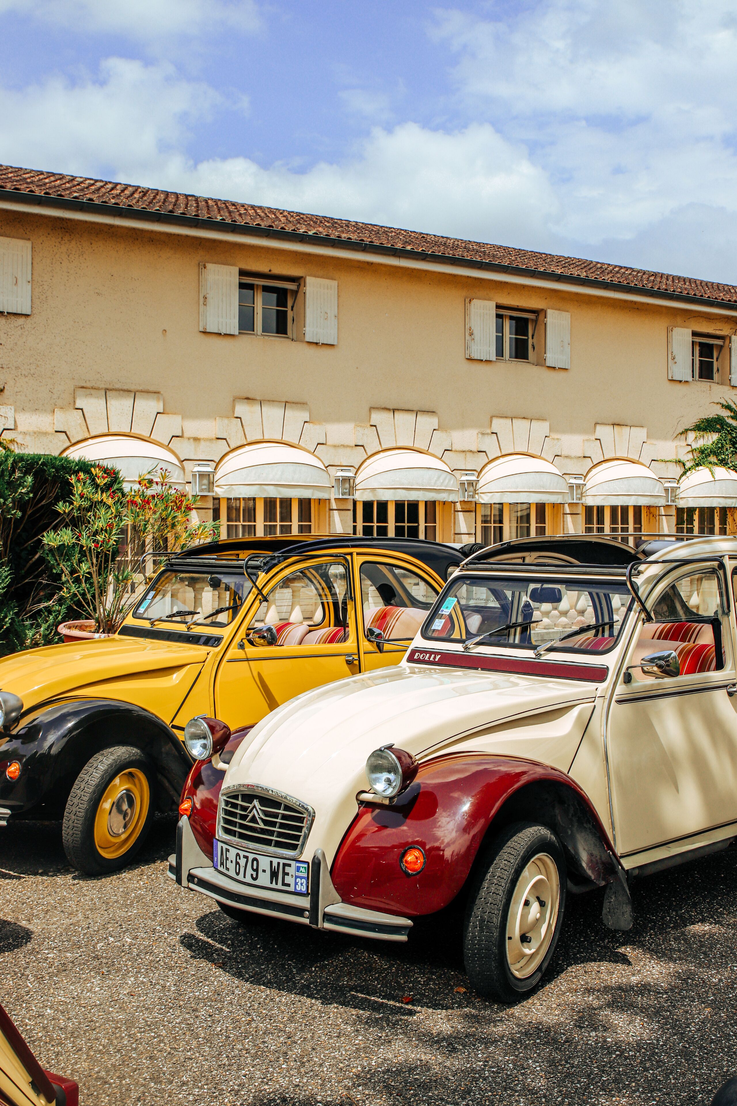 A row of vintage cars parked in front of a building with a tiled roof and multiple windows.